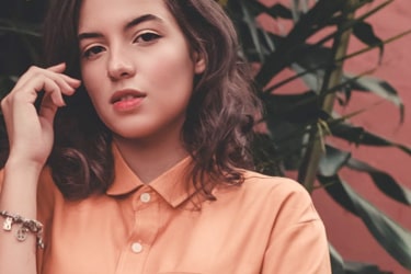 Brown haired lady wear orange shirt, greenery on the background.